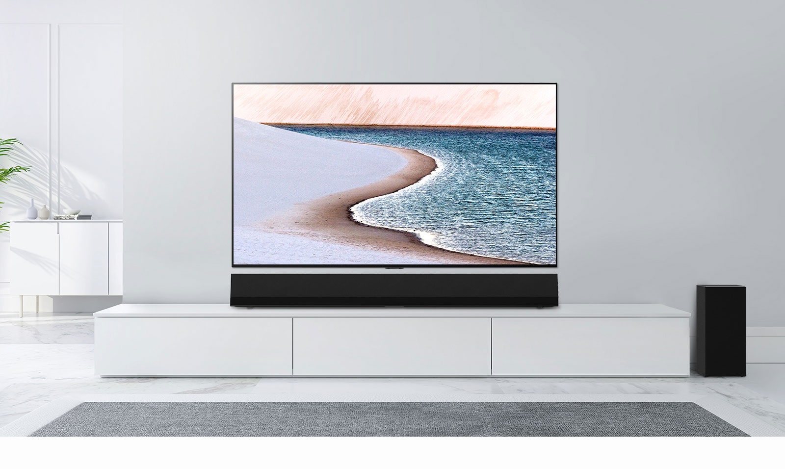 A TV is mounted on light gray wall. LG Soundbar is below it on a white cabinet. The TV shows a beach.
